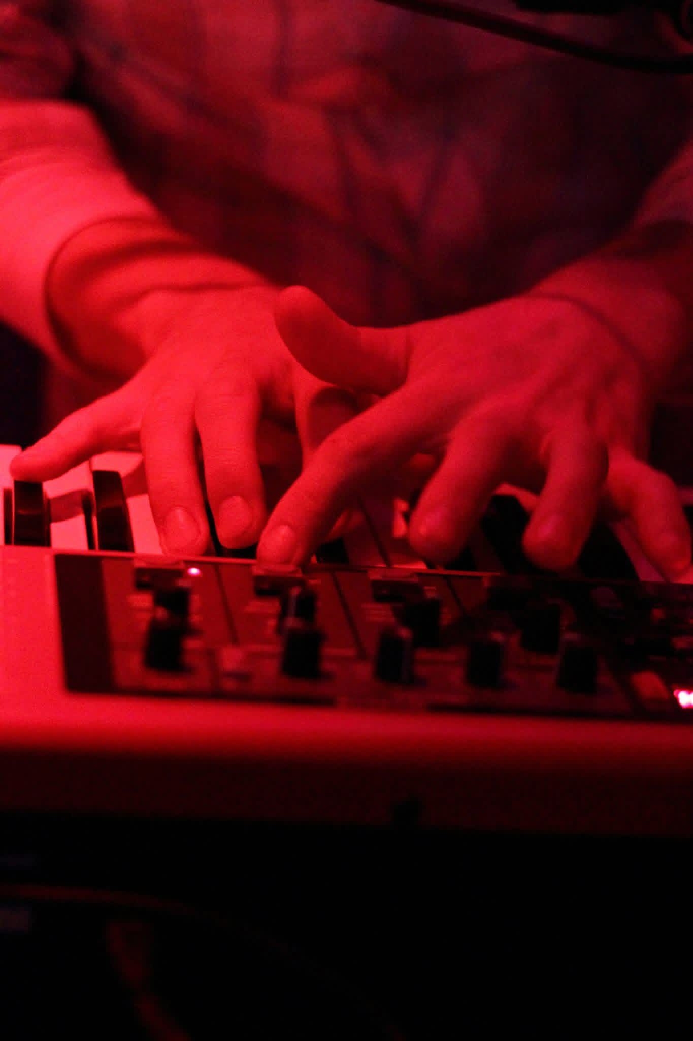 Close-up of two hands working a small synthesizer under deep red light