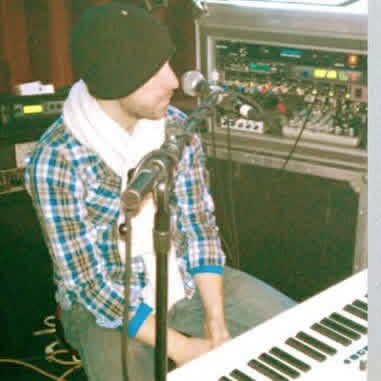 Chris LoPresto in a beanie and scarf at a mic behind a keyboard and rack gear during soundcheck