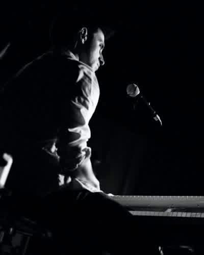 Chris LoPresto singing into a mic at the keys under a single hard side light